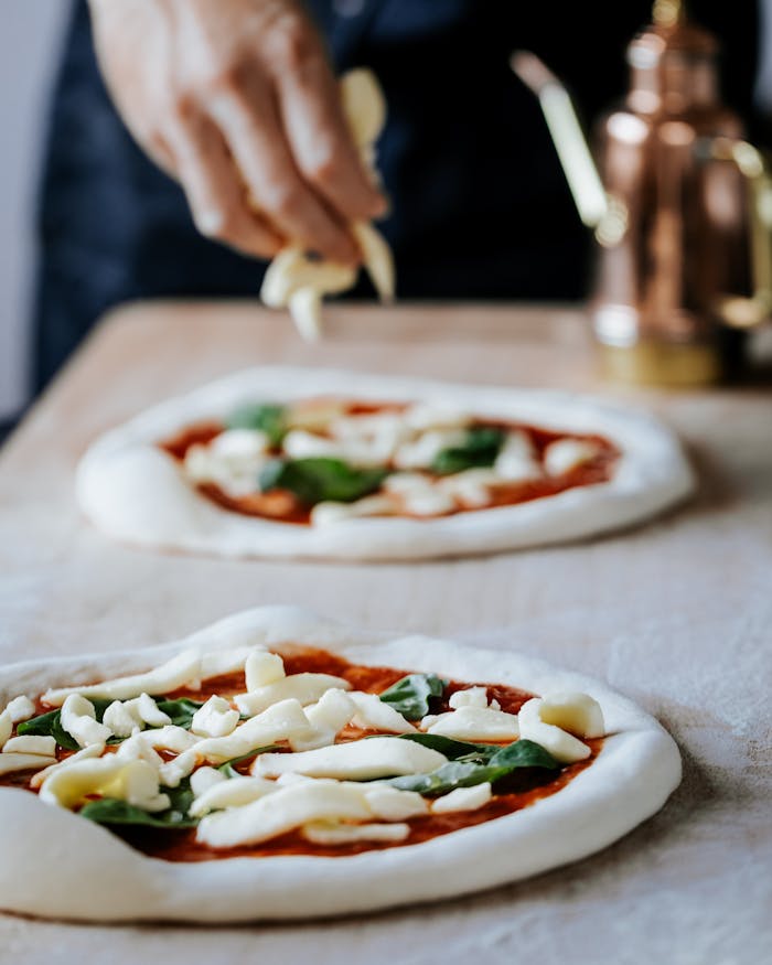 A close-up of a hand preparing Neapolitan pizza with fresh toppings in a London kitchen.