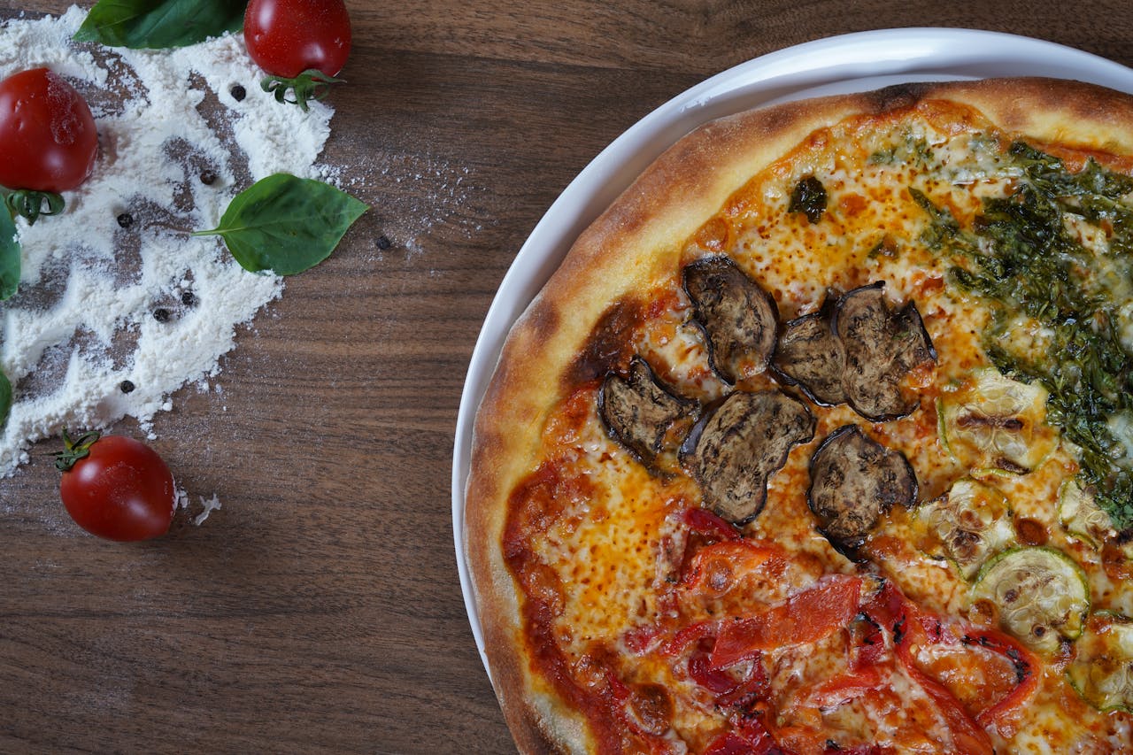 Close-up of homemade pizza with fresh vegetables and herbs on a wooden table.